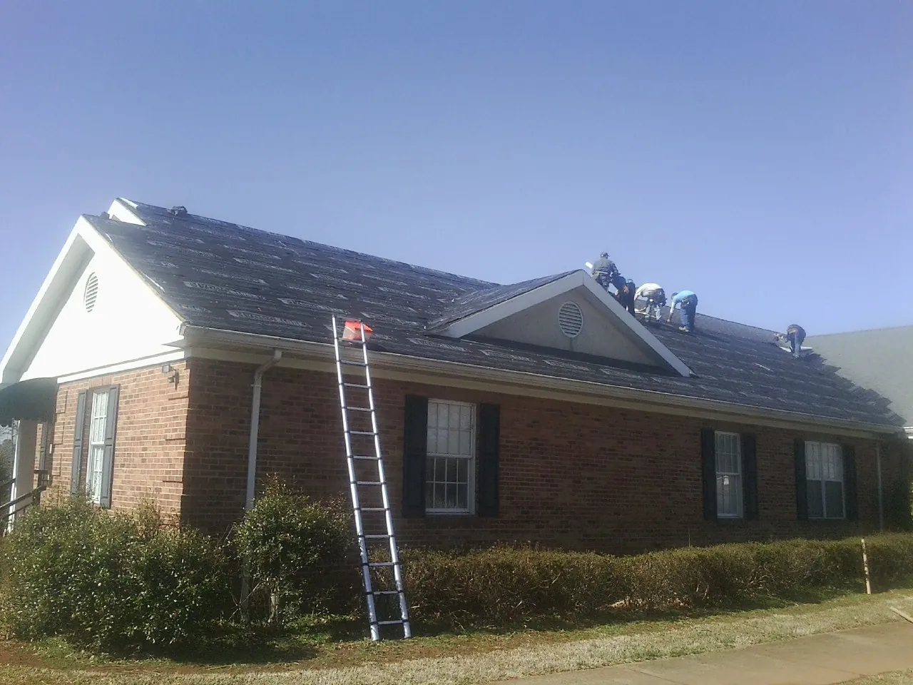 Crew tearing shingles off a brick ranch roof with a ladder set — Metal Roof Repair work by our crew in North Waterboro