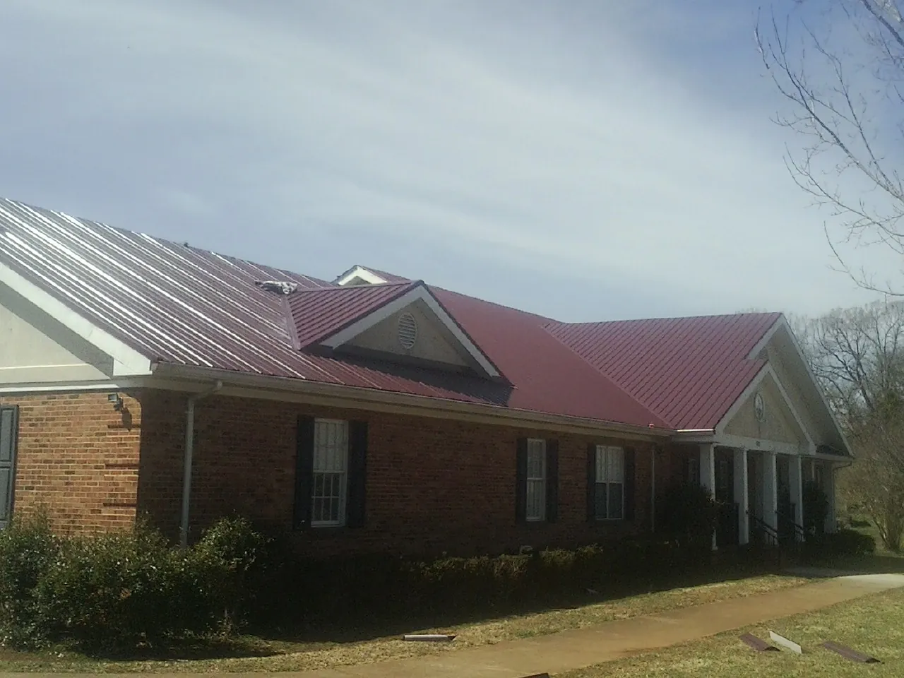 Red metal roof with gabled entries on a long brick building, from a Hail Damage Roof Repair job in North Waterboro