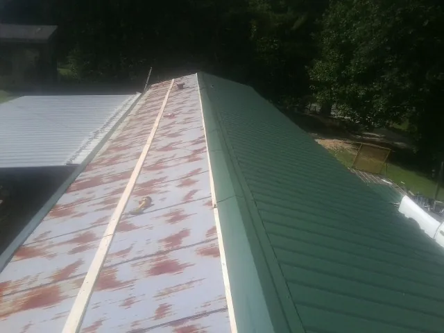 Old rusted panels beside newly installed green metal roofing — Wind Damage Roof Repair by Roofing Brothers in North Waterboro