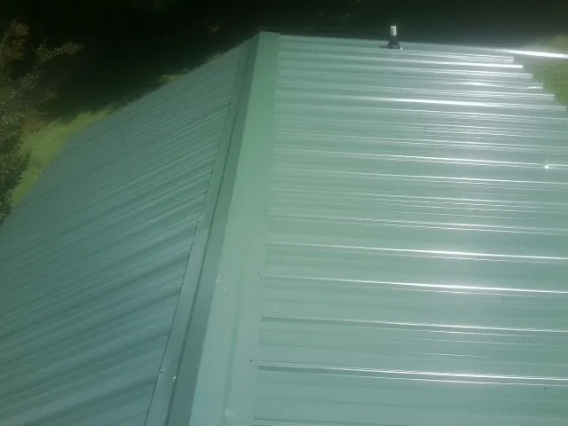 New green metal panels meeting at the ridge of a roof — Flat Roof Repair work by our crew in North Waterboro