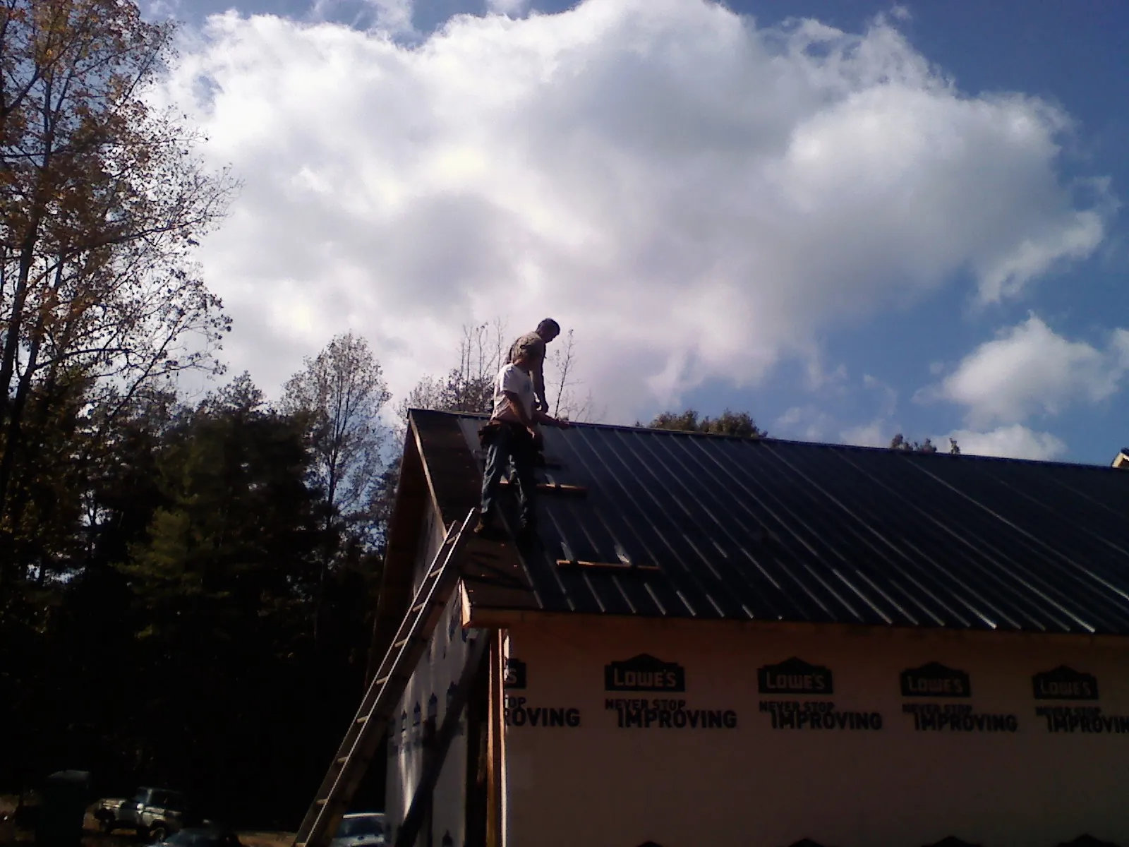Roofer fastening dark metal panels high against a cloudy sky, from a Roof Inspection job in North Waterboro