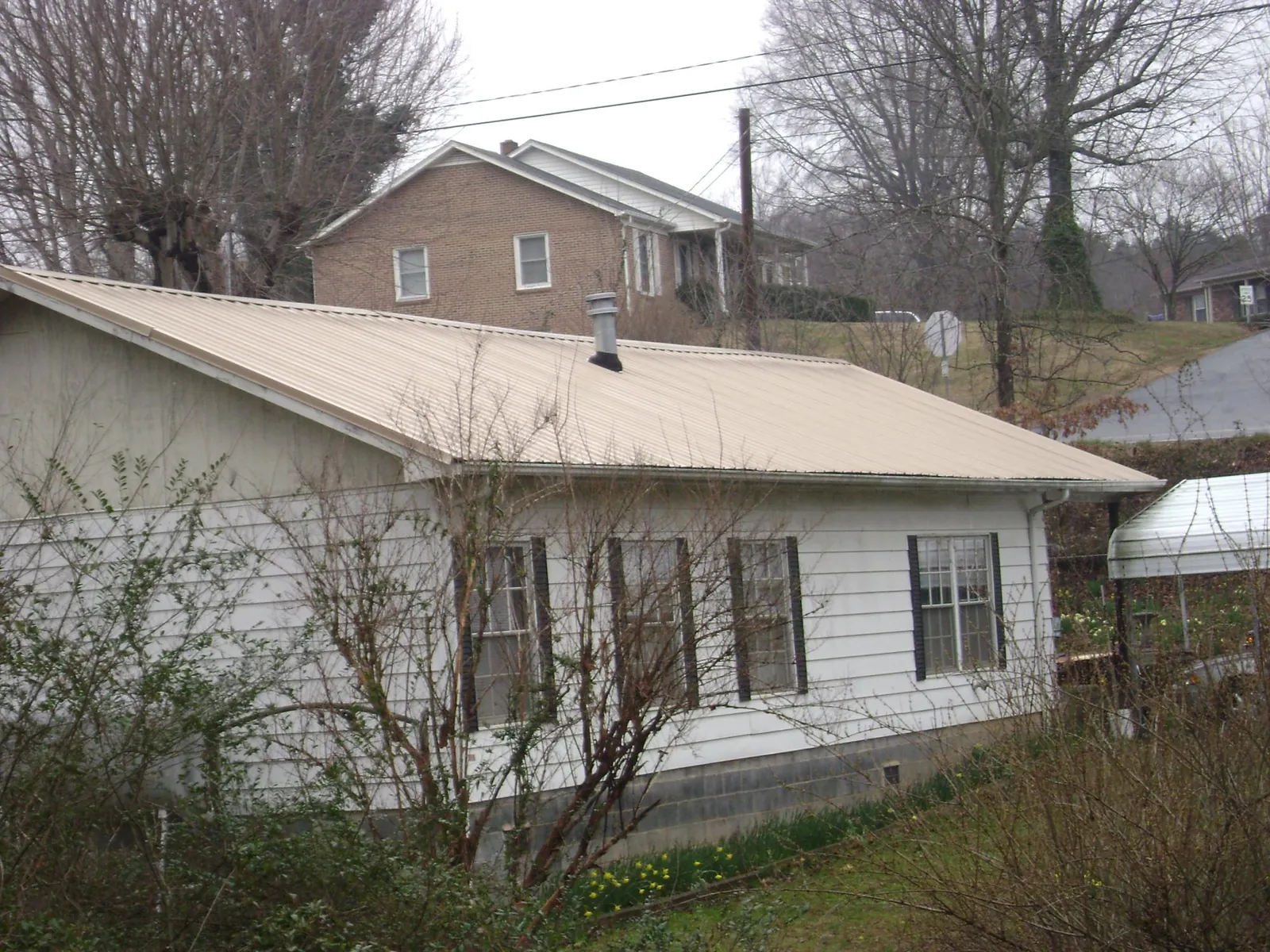 Tan metal roof on a white sided house set into a hillside — Commercial Roofing by Roofing Brothers in North Waterboro
