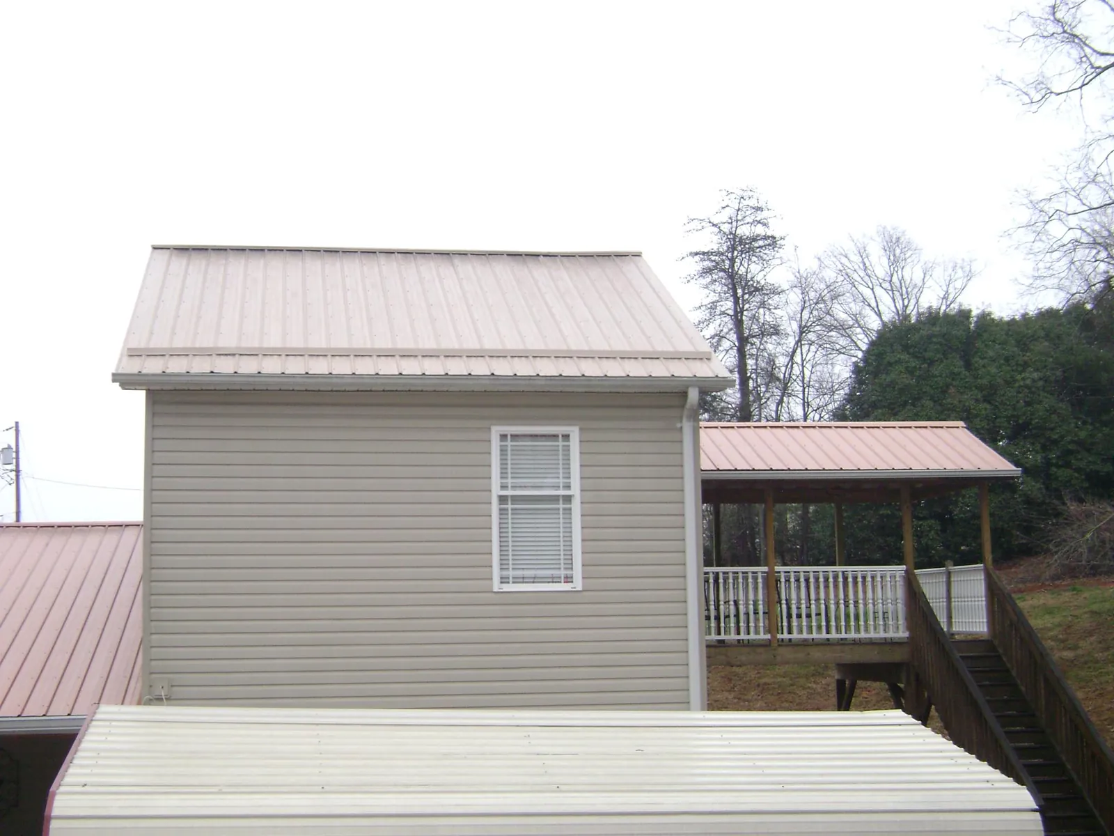 Tan metal roofs on a two story addition and attached porch, from a Roof Replacement job in North Waterboro